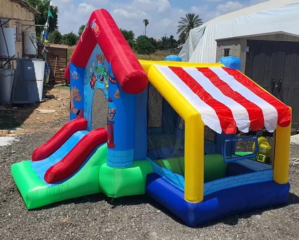 התקן קפיצה מתנפח בינוני, D2727 של Jumpy Jump, מציג עיצוב בנושא טירה עם גג פסים אדום ולבן ומגלשות כפולות. דמויות מצוירות מעטרות את החלק הקדמי. הוא ממוקם בחוץ עם עצי דקל, שמיים כחולים, חצץ מתחת לרגליים, ליד אוהל לבן ובניינים.