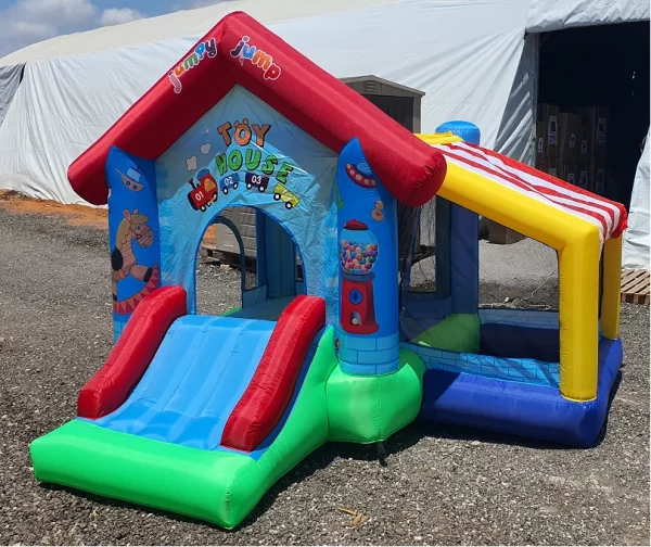 בית הקפצה מתנפח בשם "בית הצעצוע" מאת Jumpy Jump כולל מגלשה, בריכת כדורים ופאנלים צבעוניים עם איורים מצוירים. הוא ניצב בחלקו מעל חצץ ליד מבנה לבן בחוץ.