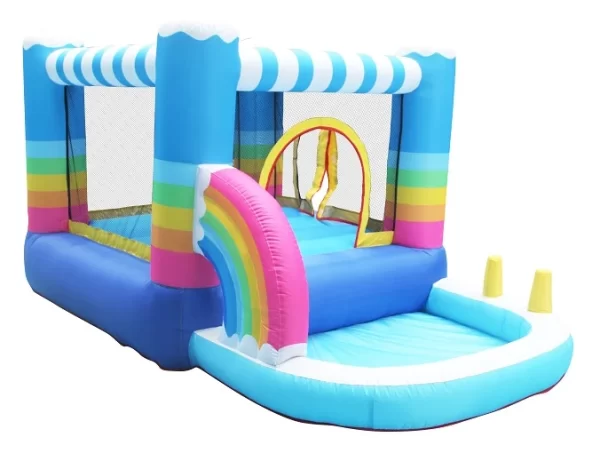 התקן קפיצה מתנפח בינוני | JUMPER | בריכת שעשועים מציגה עיצוב צבעוני, כחול, לבן ופסי קשת בענן עם מגלשה בצורת U עם קשת בענן. הוא כולל שני קונוסים צהובים בכניסה וקירות צד רשת לניראות.